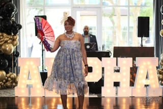 A guest walking the floor with a hand fan in front of lit ALPHA letters