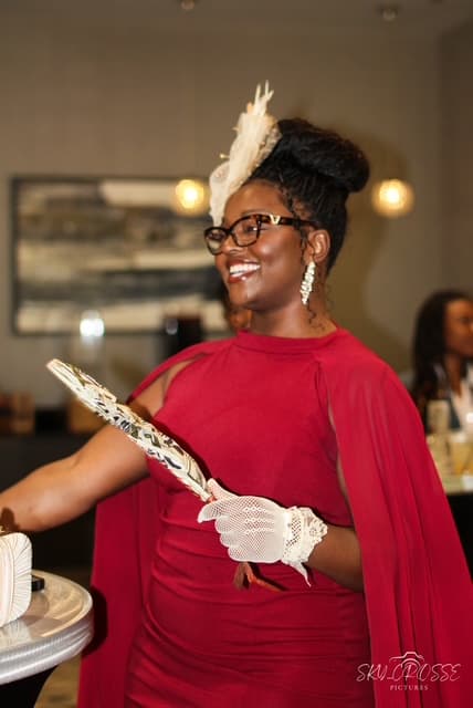 A guest in a red dress with a cream feather fascinator, lace gloves and a hand fan