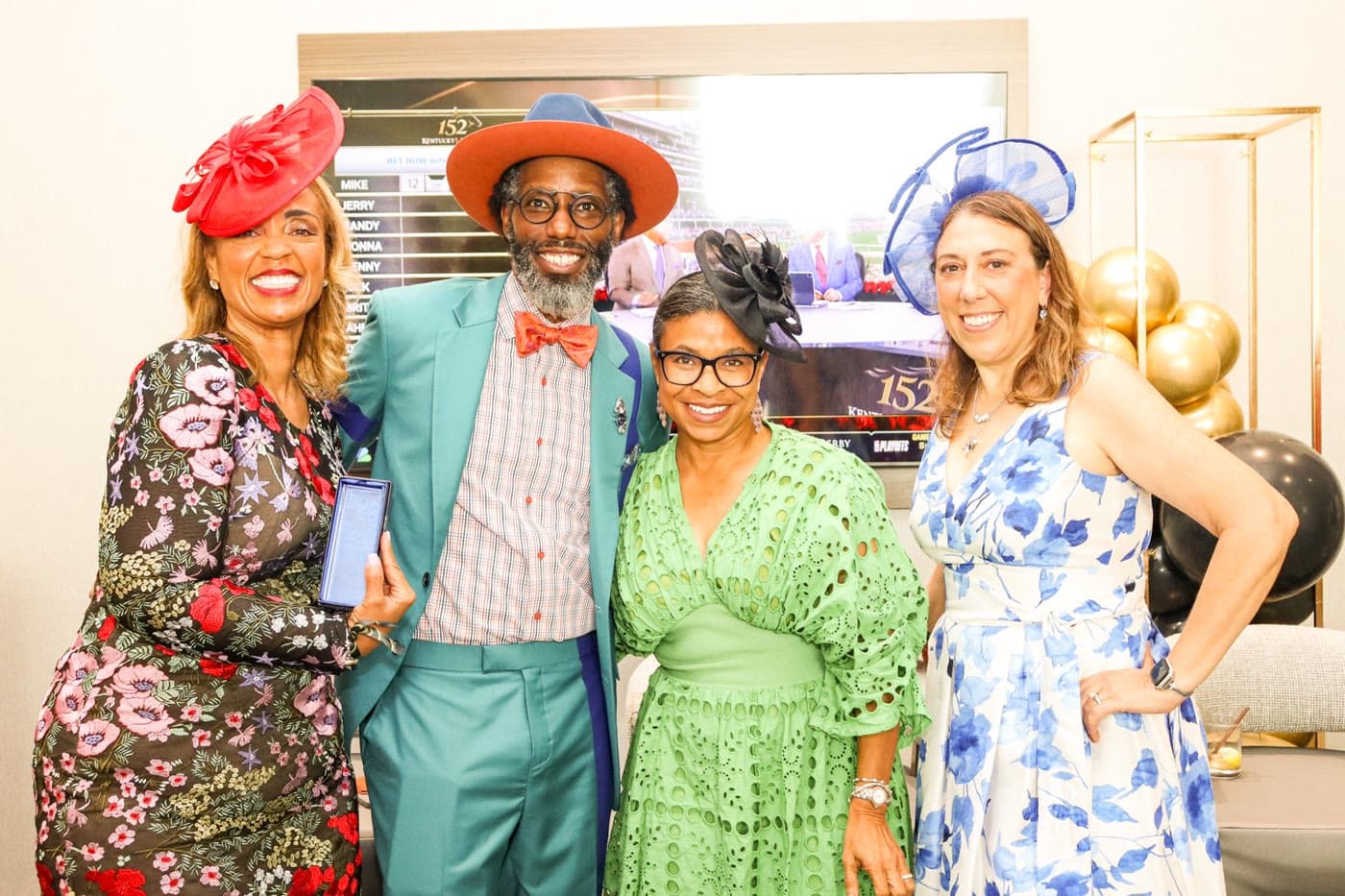Four guests in Derby hats and fascinators in front of a screen showing the Kentucky Derby