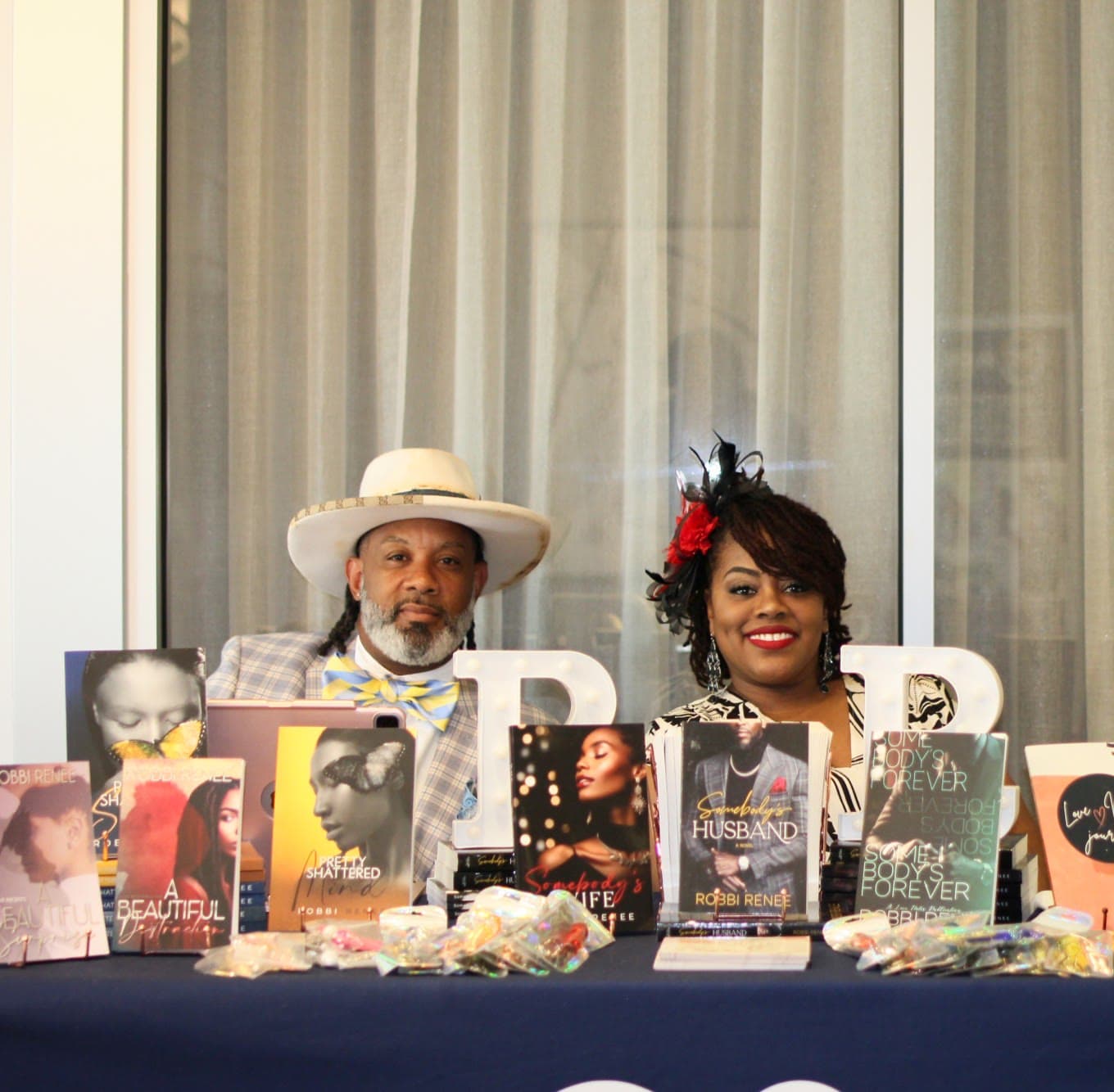 An author and a vendor behind a table of books and jewellery at the marketplace